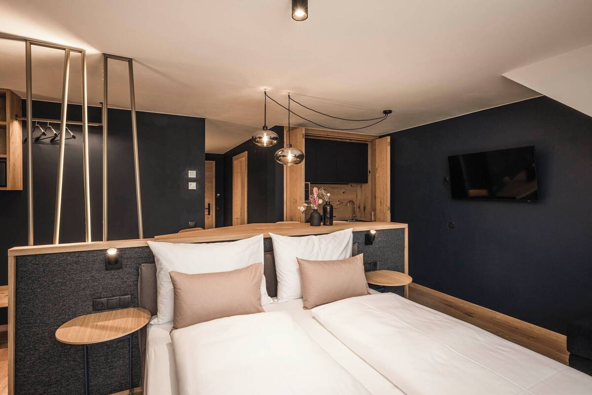 Ein modernes Schlafzimmer mit Bett, Nachttischen, einem Spiegel und einem an der Wand montierten Fernseher.