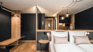 Habitación de hotel moderna con pared de acento de madera, una mesita redonda, cama con ropa blanca y una zona de kitchenette.