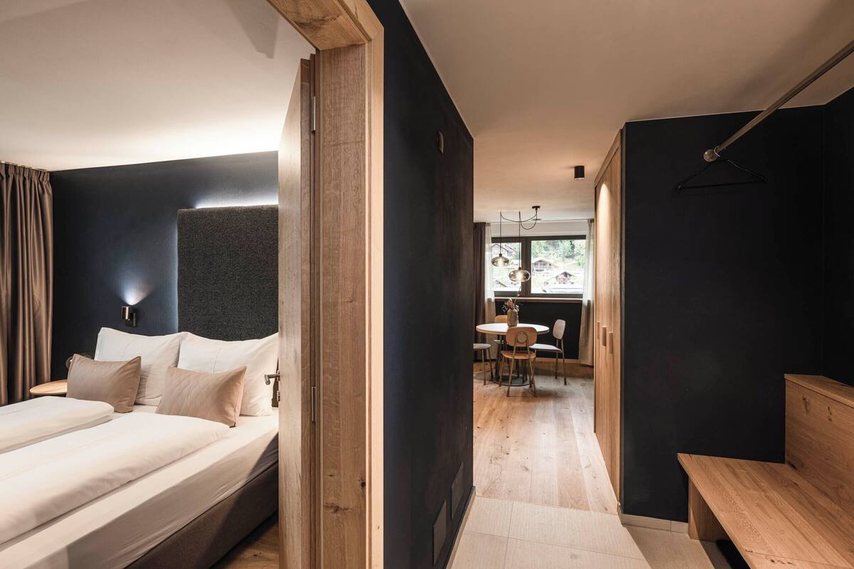 Ein modernes Hotelzimmer mit einem großen Bett, einer hölzernen Bank und einem Essbereich mit Tisch und Stühlen.