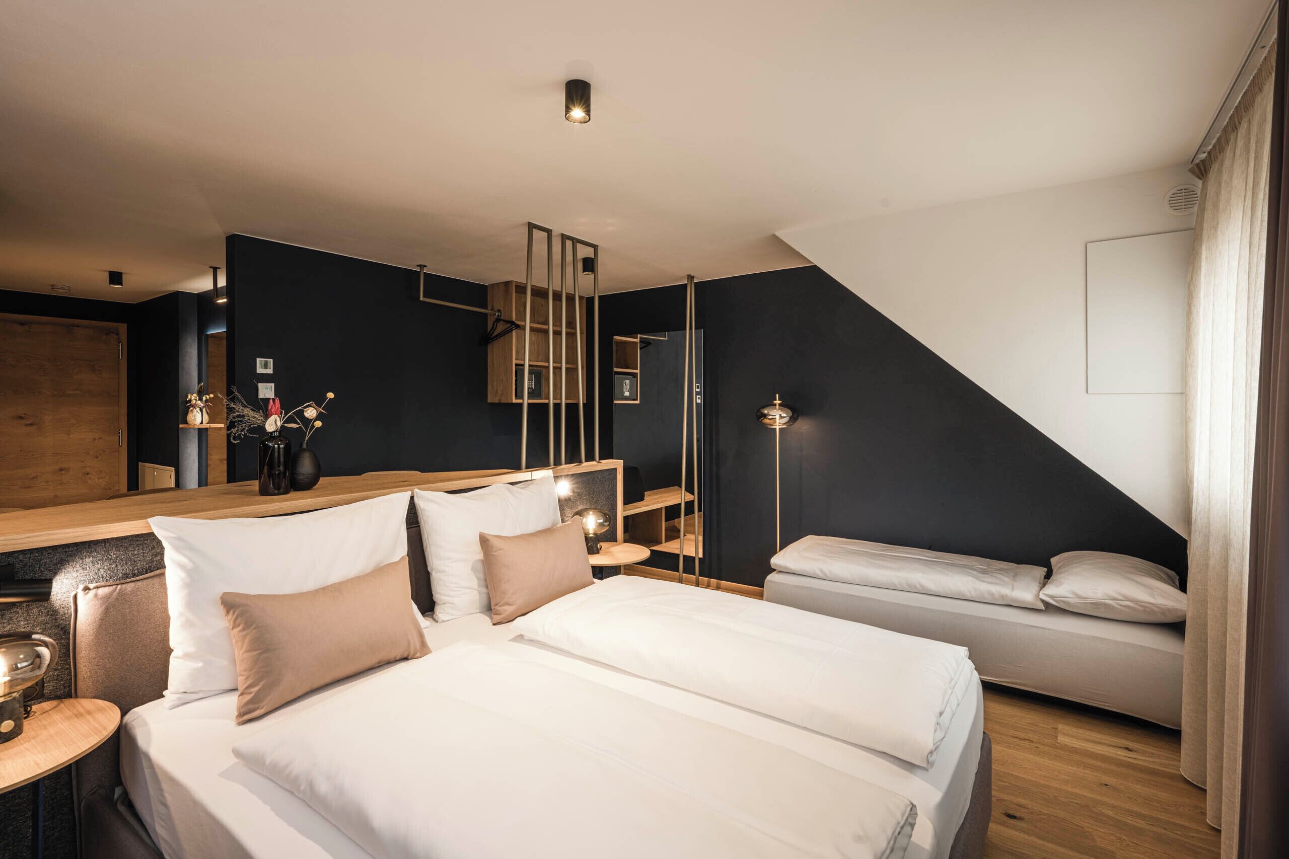 Ein modernes Hotelzimmer mit einem großen Bett, einem kleineren Bett, einem Schreibtisch und einem Spiegel.