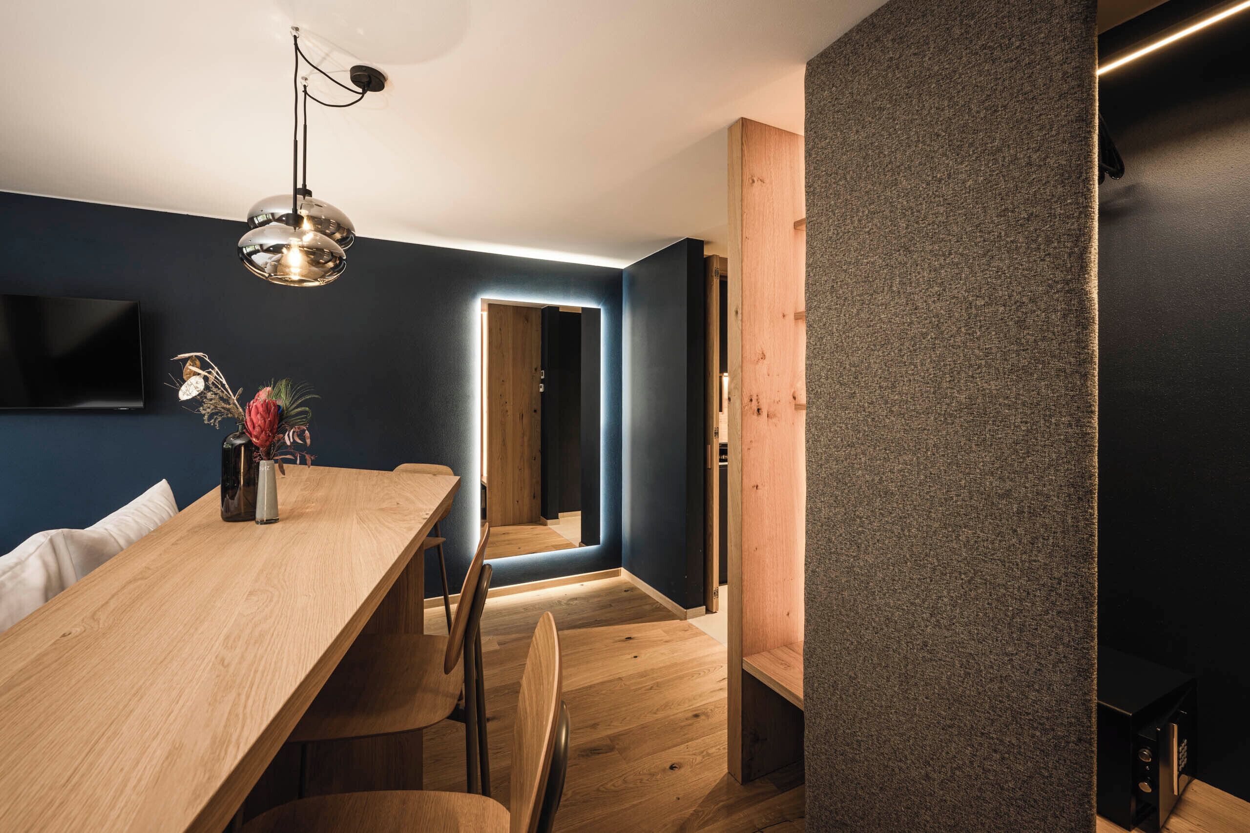 Uma sala de jantar moderna com uma mesa e cadeiras de madeira, uma luminária pendente e uma televisão na parede.