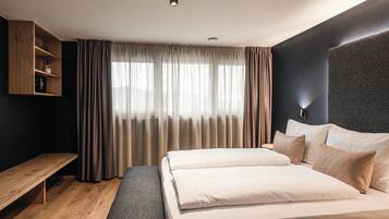 A modern hotel room with a large bed, a bench, a wooden shelf, and a large window with curtains.