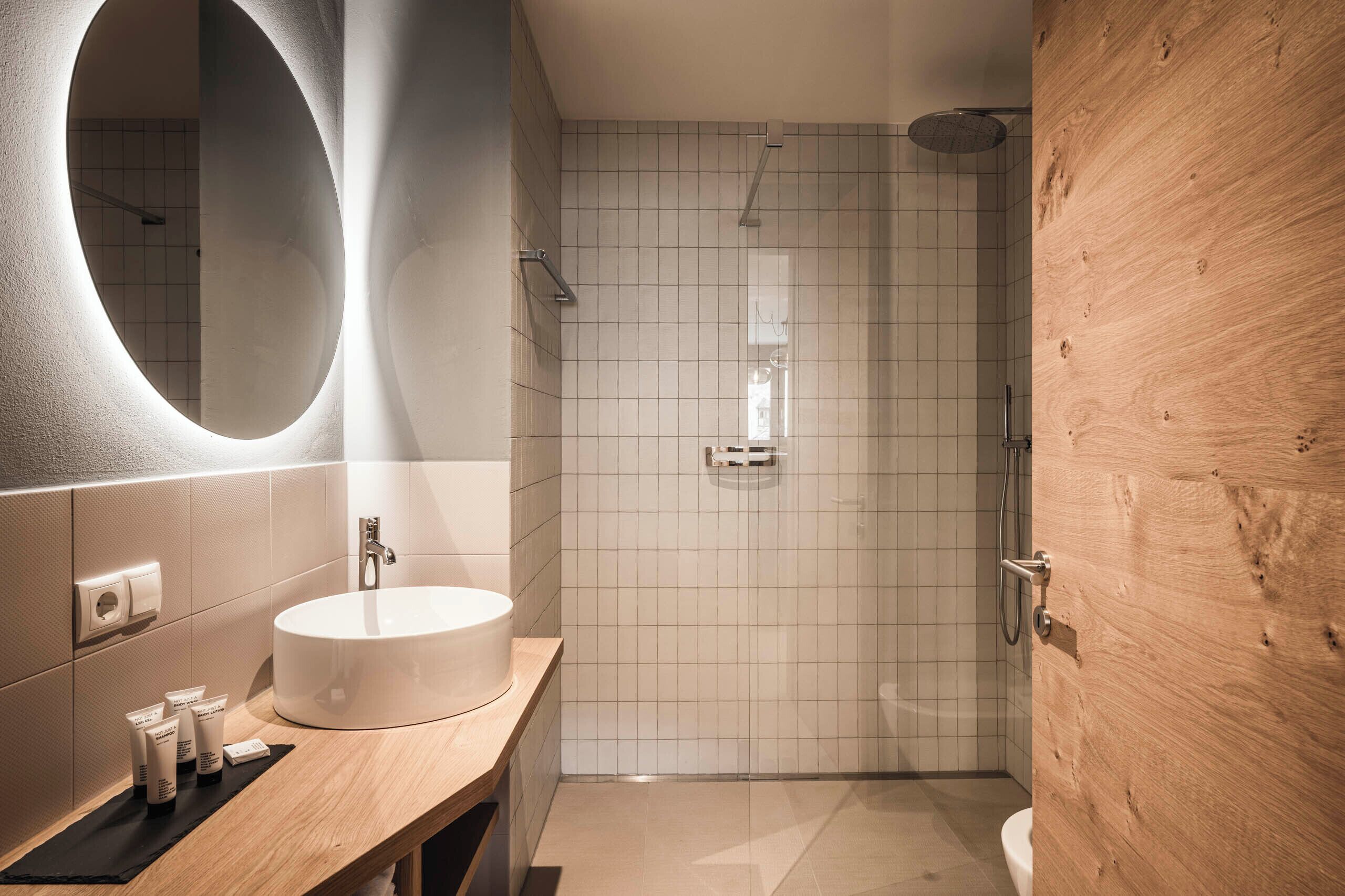 Une salle de bain moderne avec un grand miroir rond, un lavabo et une douche.