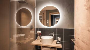 A modern bathroom with a glass-enclosed shower, a round mirror, and a wooden vanity with a sink.