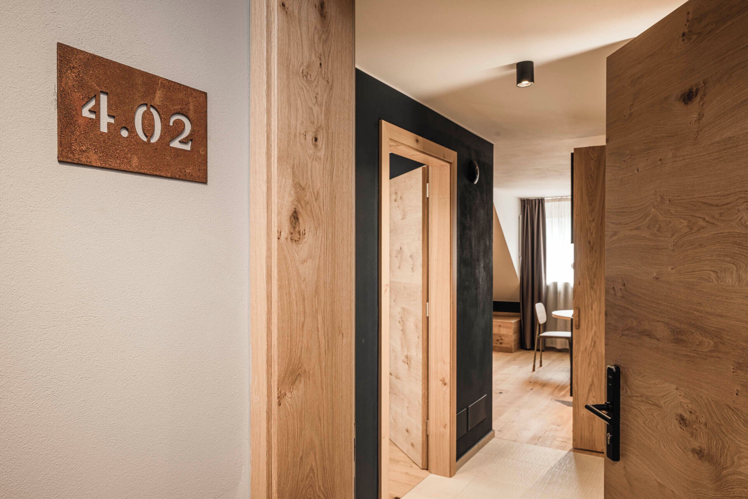Een modern interieur met een houten deur, een nummerbord en een kijkje in een kamer met een stoel en een tafel.
