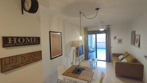 A living room with a sofa, a dining table, and a TV. There are wall decorations and a ceiling light. - La Envía - Beautiful apartment with terrace, swimming pool, luminous (La Envía)