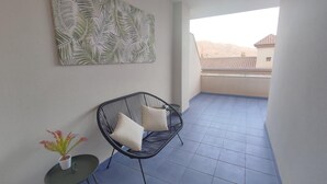 A balcony with a black wire chair, two white cushions, a small table with a potted plant, and a large leaf-patterned artwork on the wall. - La Envía - Beautiful apartment with terrace, swimming pool, luminous (La Envía)