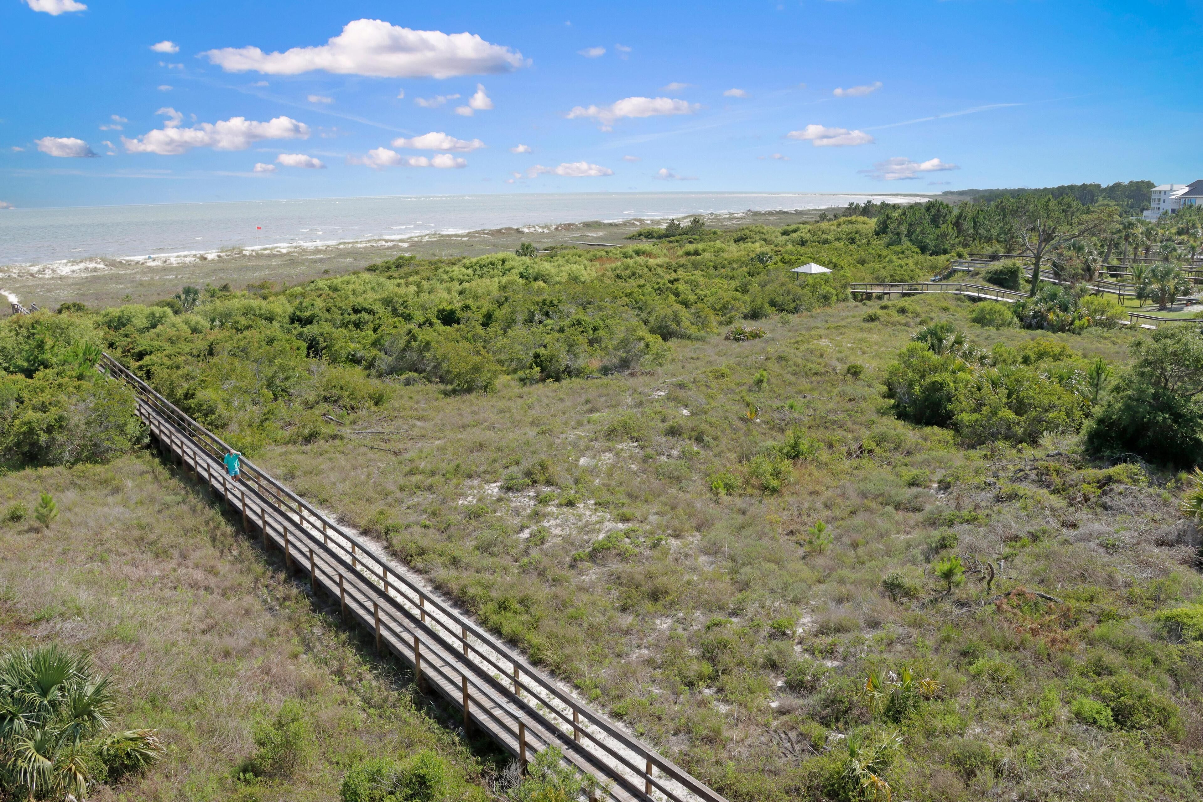 A wooden boardwalk leading to a beach area with dense greenery and a clear view of the ocean.