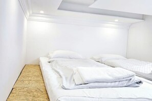 A neatly made bed with white linens and pillows, a wooden floor, and a white ceiling with recessed lighting. - FEE Apartment Berlin 2 (Berlin)