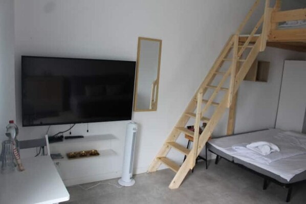 A room with a TV mounted on the wall, a wooden ladder, a bed, and a small table with a bottle and a remote control. - FEE Apartment Berlin 2 (Berlin)