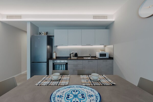 Una cocina compacta equipada con refrigerador, microondas y estufa, y un comedor con dos sillas y una mesa.