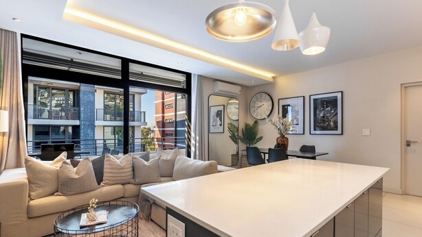 Un salon moderne doté d’un grand îlot central, d’un canapé agrémenté de nombreux coussins, d’une table basse et d’un coin repas avec une table et des chaises.