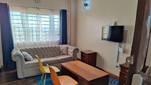Ein Wohnzimmer mit einer Couch, zwei Sesseln, einem Holztisch und einem an der Wand befestigten Fernseher.
