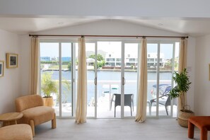 Il s’agit d’une pièce spacieuse dotée d’une grande porte-fenêtre coulissante qui donne sur un balcon offrant une vue sur un port de plaisance et des immeubles. La pièce contient deux chaises et une petite table.