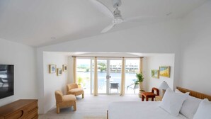 Un dormitorio con cama, escritorio, dos sillas, televisor y vista al exterior.