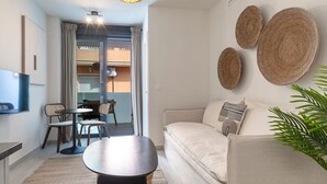 Una sala de estar moderna con un sofá, una mesa redonda de centro y un televisor montado en la pared. Hay cestas tejidas en la pared y una planta en maceta en el suelo.