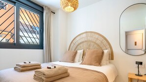Un dormitorio con cama, mesita de noche, espejo y ventana con cortinas.