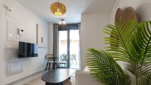 Una sala de estar moderna con televisor de pantalla plana, una mesa de comedor, sillas, una planta grande en maceta y una lámpara de techo.
