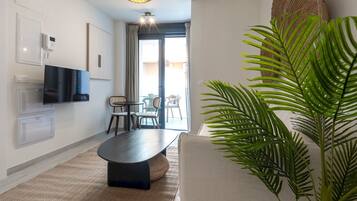 En moderne stue med et fladskærms-tv, et spisebord, stole, en stor stueplante og en loftlampe.