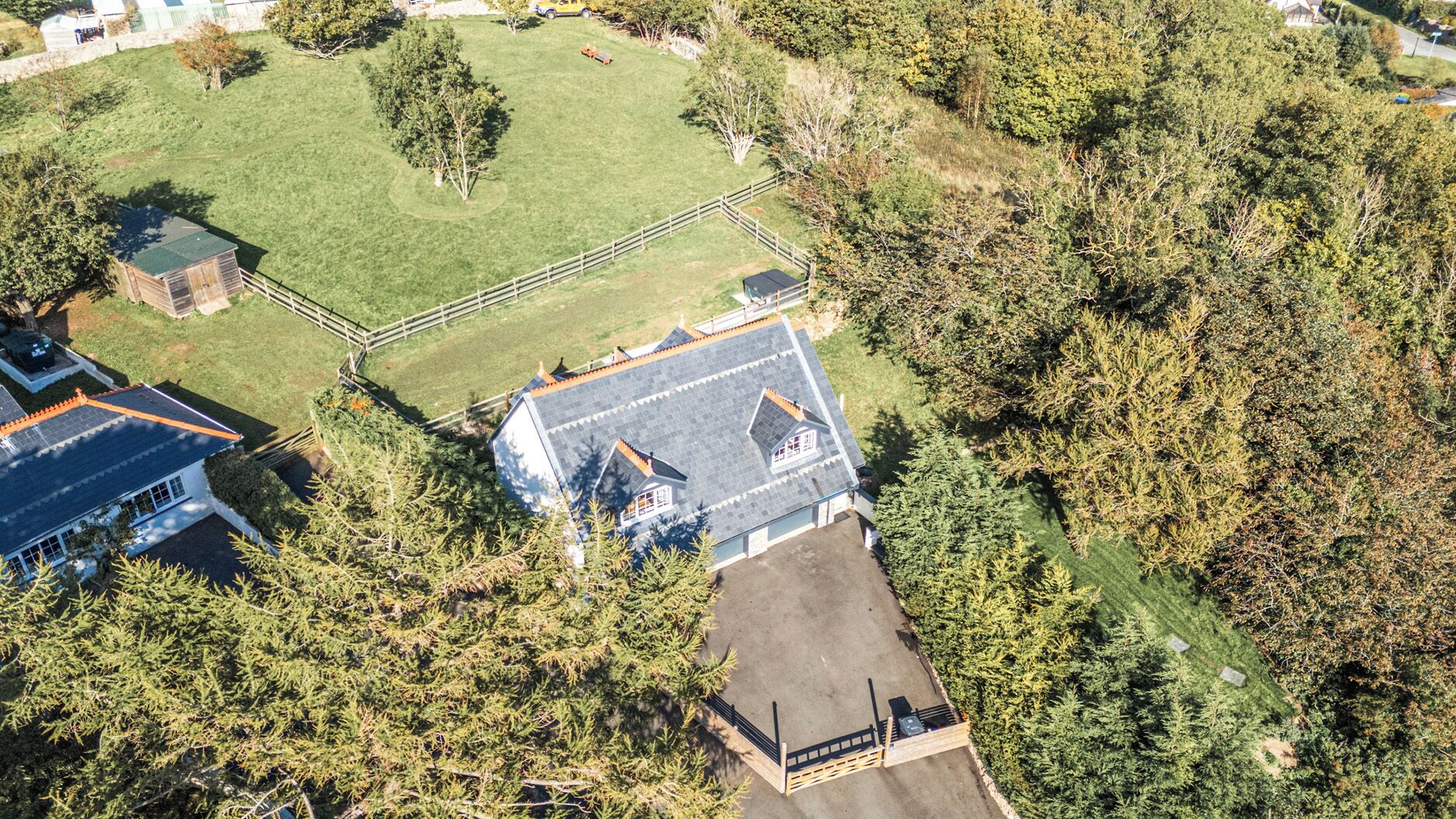 Vista aérea de una zona residencial que muestra una casa con techo inclinado, patio cercado y abundante vegetación.