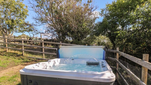 A hot tub with a wooden bench, surrounded by a wooden fence and trees. - The Gatekeepers Cottage - Skerry Vore (Llandudno Junction)