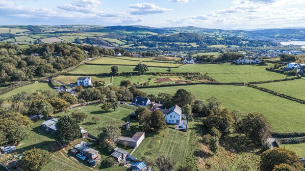 Une vue aérienne d’une zone rurale, avec des maisons dispersées, des champs et un petit plan d’eau au loin.
