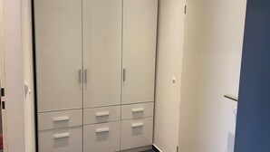Quarto com um guarda-roupa branco grande, uma porta e chão de azulejos.