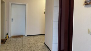 Um corredor com uma porta branca, uma porta de madeira e um chão de azulejos.