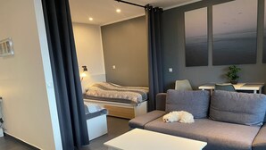 Uma sala de estar moderna com sofá, mesa pequena, cama com manta e planta em vaso.