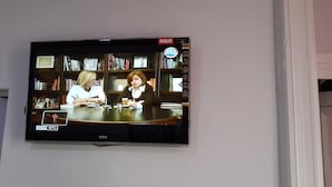 Een flatscreen-tv aan de muur met een afbeelding van twee personen zittend aan een tafel in een kamer met boekenkasten.