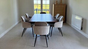 Comedor con una mesa grande, seis sillas, un aparador de madera y una ventana con vistas a un jardín.