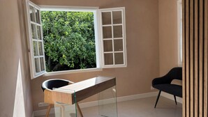 Una habitación con escritorio, una silla y ventana con vistas a zonas verdes.