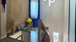 Un interior moderno con una escalera de cristal, una pared azul decorativa y un elemento de iluminación ornamental.