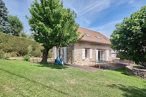 A stone house with a wooden deck, a large tree, and a clear blue sky.