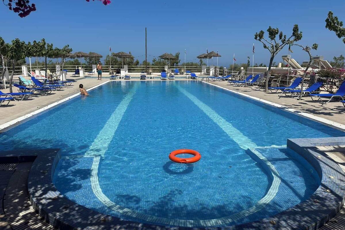 A swimming pool with blue water, surrounded by lounge chairs and a lifebuoy.