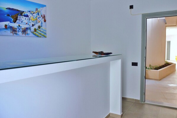 A reception desk with a glass top and a painting of a coastal scene. - Lovely Hot-L (Santorini)