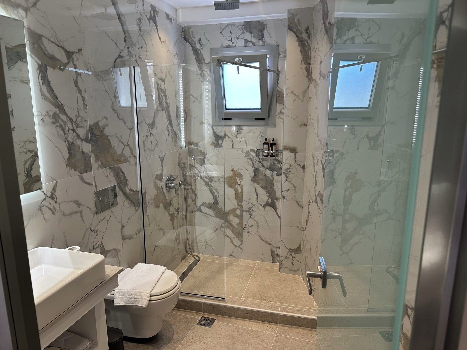 A bathroom with a glass-enclosed shower, a toilet, and a sink.