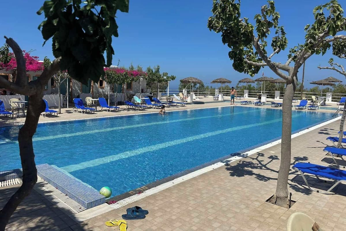 A swimming pool with blue chairs, a tiled deck, and a clear sky.