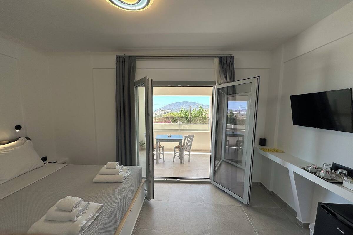 A hotel room with a bed, a desk, a TV, and a balcony with a table and chairs.