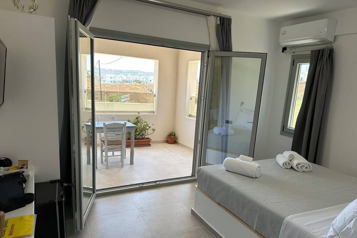 A hotel room with a bed, a desk, a chair, and a balcony with a view.