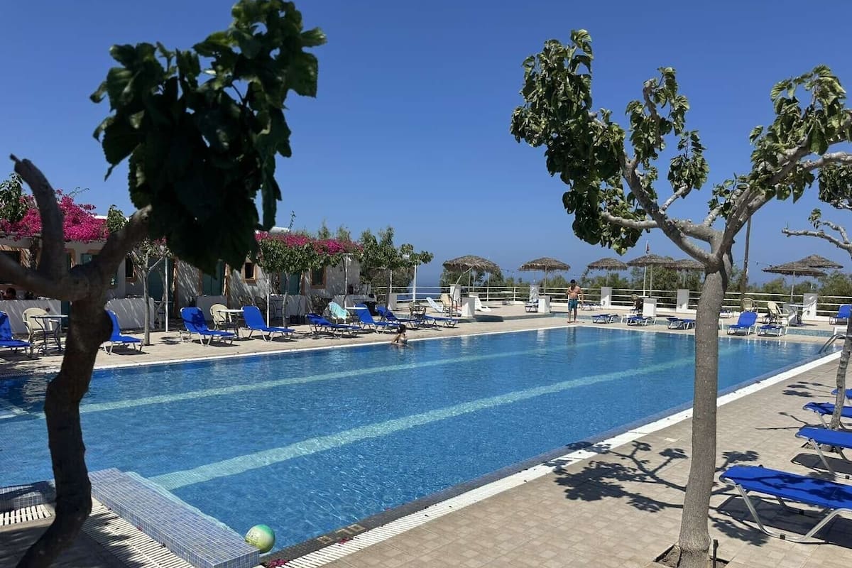 A swimming pool with blue chairs, a clear sky, and a view of the sea.