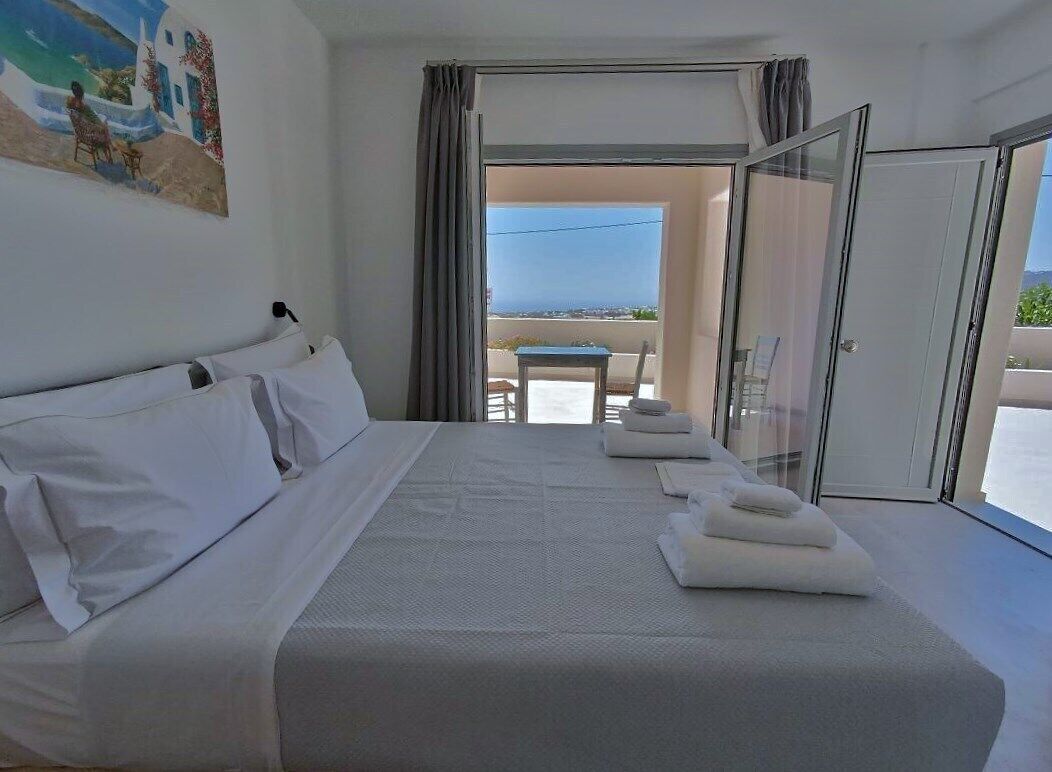 A hotel room with a large bed, a balcony with a table and chairs, and a view of the sea.
