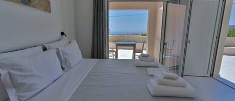 A hotel room with a large bed, a balcony with a table and chairs, and a view of the sea.