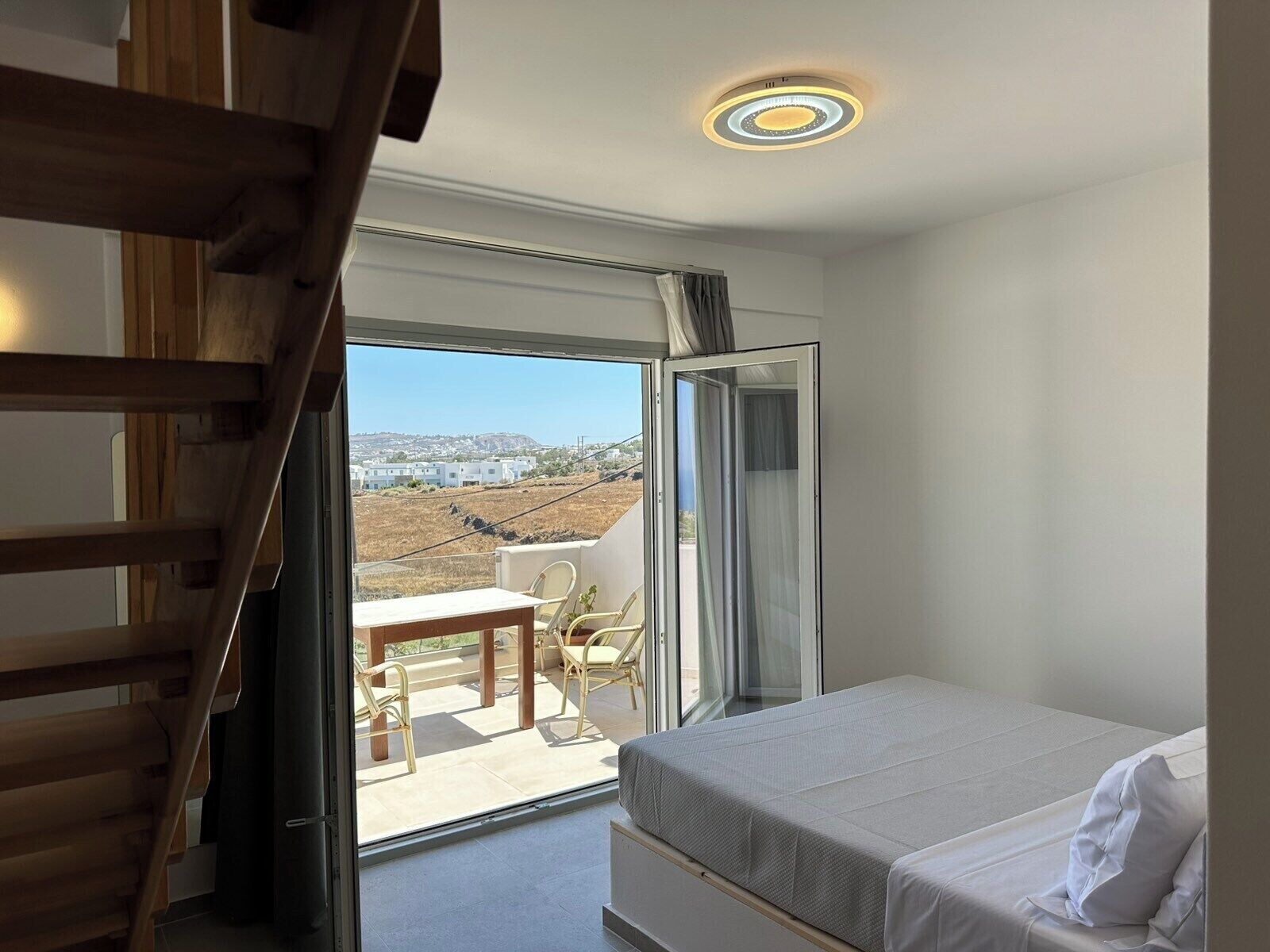 Une chambre à coucher avec un lit, une table et des chaises sur un balcon offrant une vue sur des immeubles et un paysage.