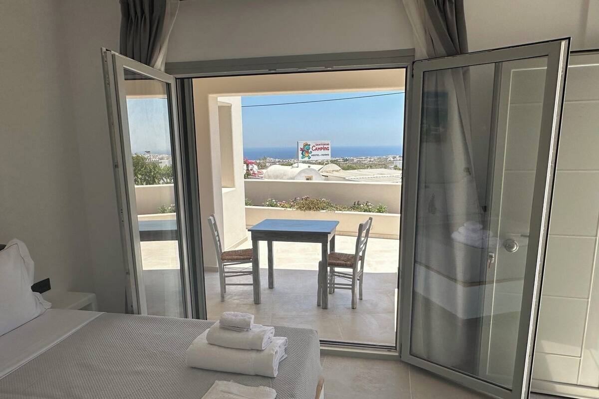 A hotel room with a bed, a table, and chairs on a balcony with a view of the sea.