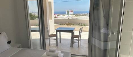 A hotel room with a bed, a table, and chairs on a balcony with a view of the sea.