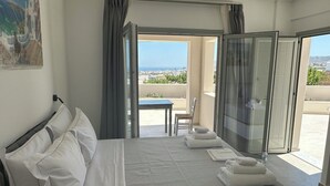 A hotel room with a bed, a table with chairs, a balcony with a view, and a painting on the wall. - Lovely Hot-L (Santorini)