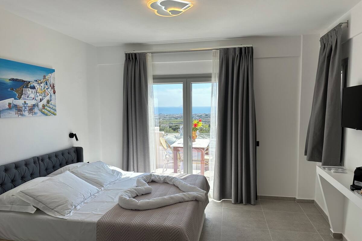 A bedroom with a bed, a TV, and a balcony with curtains.