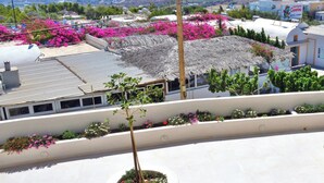 A coastal hotel with a rooftop garden, a thatched roof, and a view of the sea and cityscape. - Lovely Hot-L (Santorini)