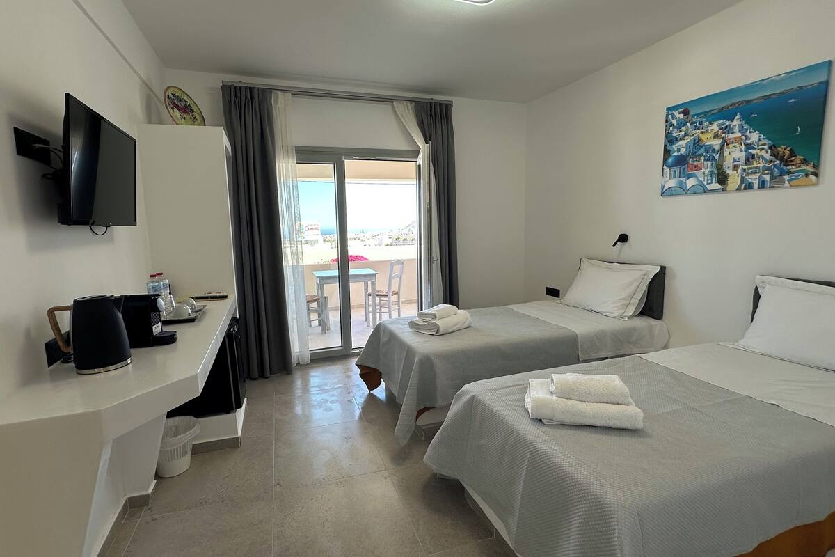 A hotel room with two beds, a TV, a desk with a coffee maker, and a painting on the wall.